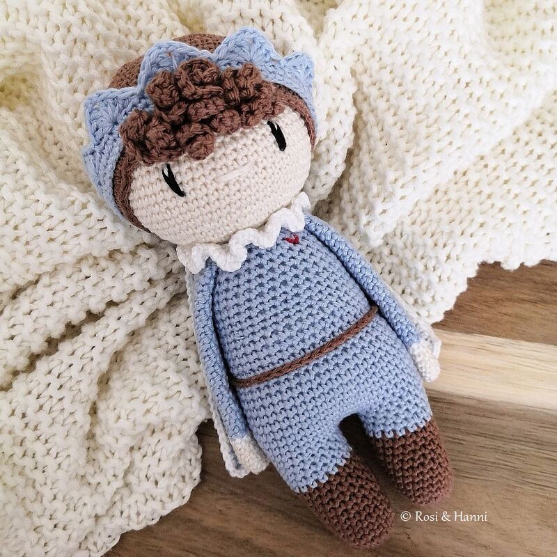 Gehäkelte Amigurumi-Puppe in hellblau und braun auf weißer Strickdecke
