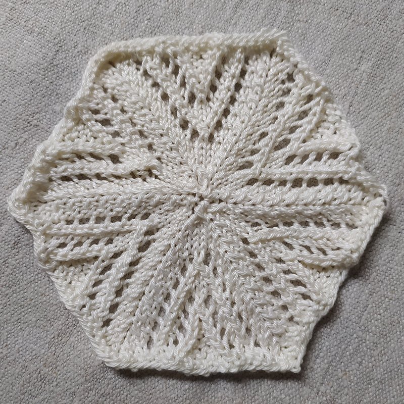 Weiße sechseckige Strickapplikation mit Ajourmuster auf hellem Untergrund
