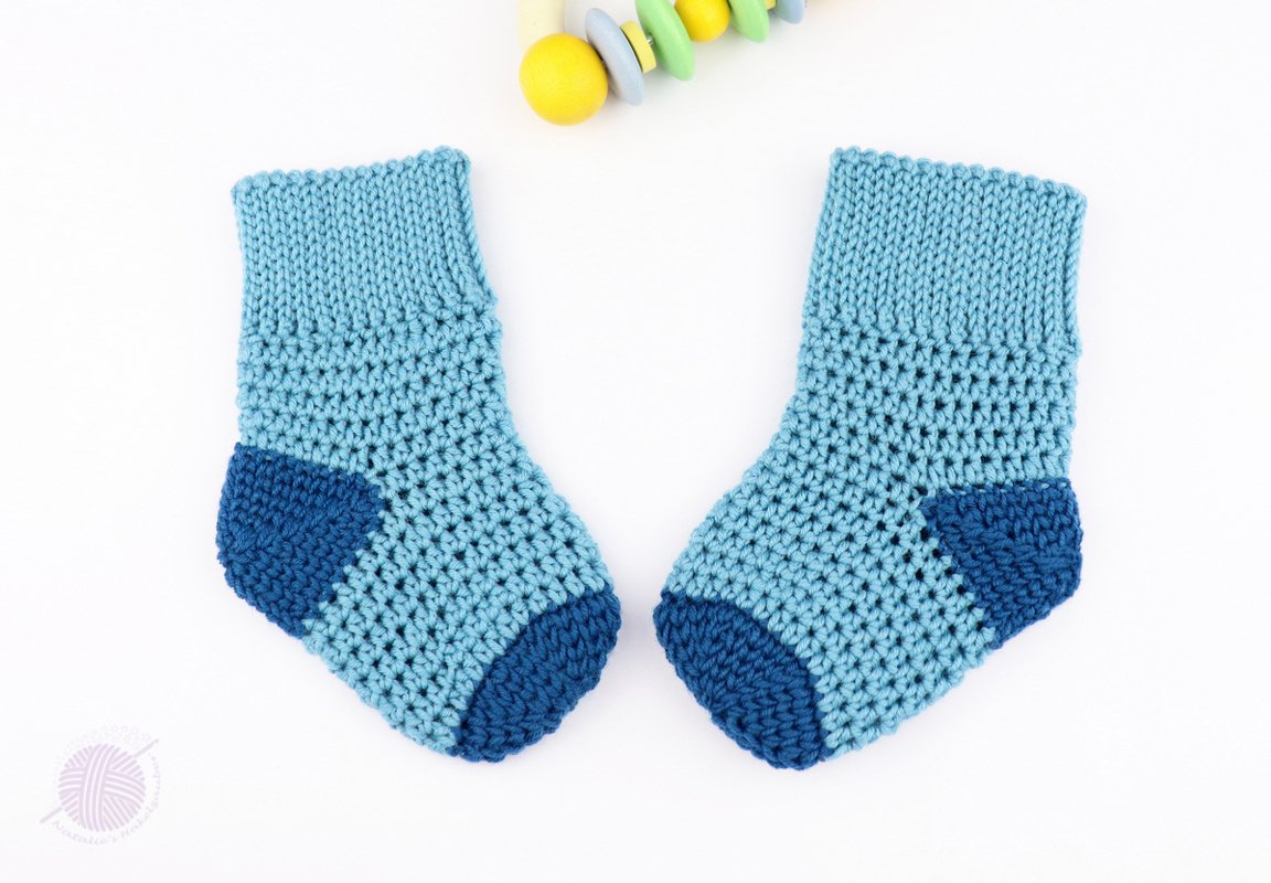 Flat-lay of textured light-blue crochet baby socks showing ribbed cuff and dark-blue heel and toe
