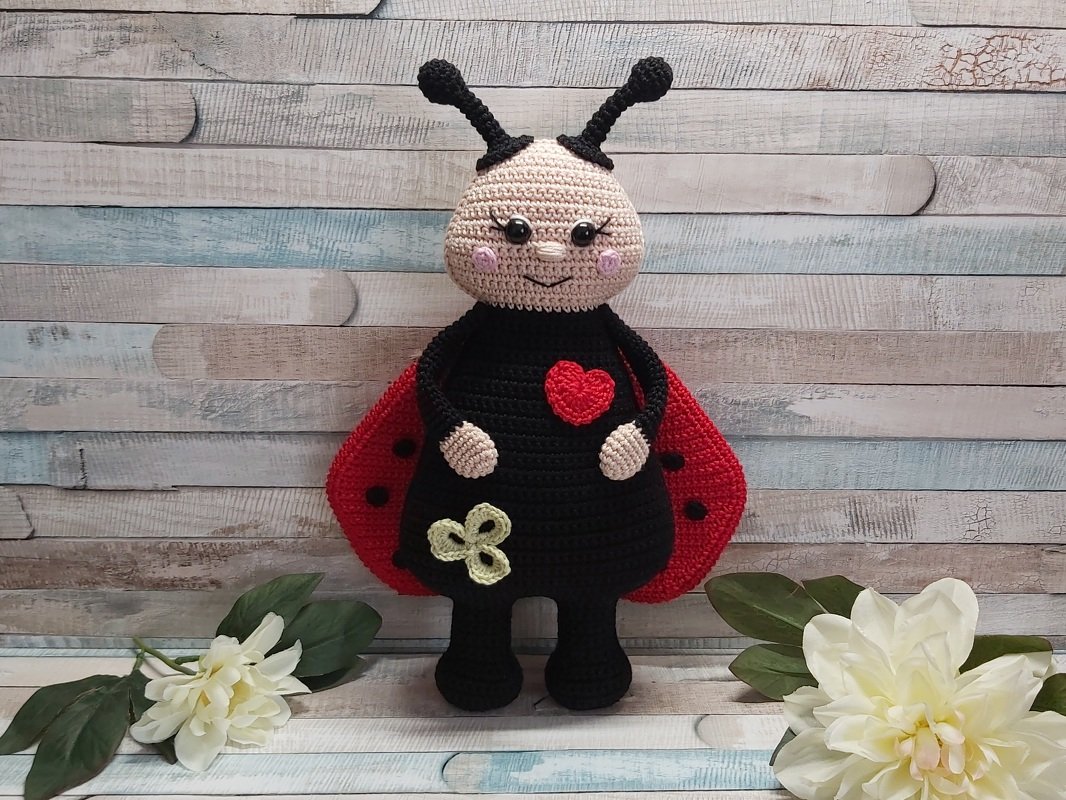Gehäkeltes Marienkäfer-Amigurumi mit roten Flügeln, Herz und kleinem Kleeblatt