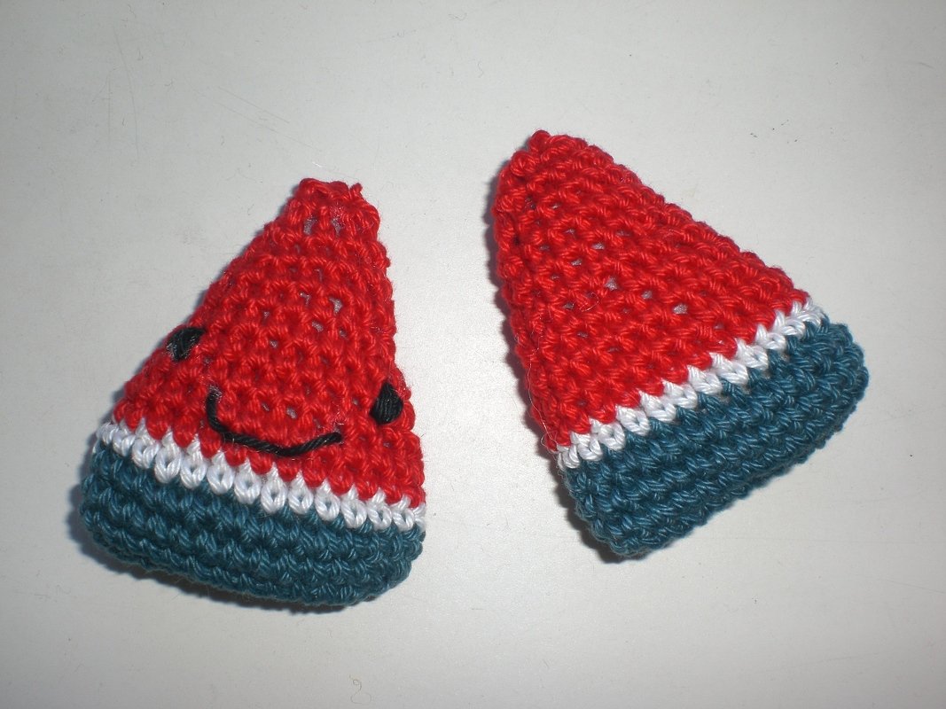 Zwei gehäkelte Mini-Wassermelonen, rot mit weißem Streifen und grünem Rand, eines mit aufgesticktem Gesicht