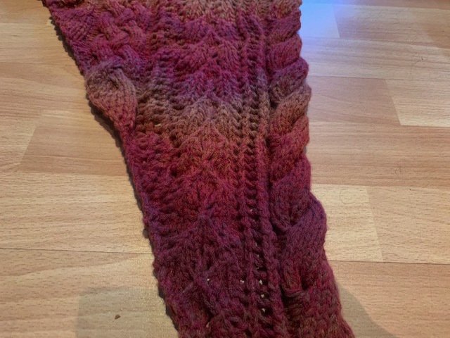 Gestricktes Dreieckstuch mit Zopfmuster und Rot-Braun-Farbverlauf auf Holzboden