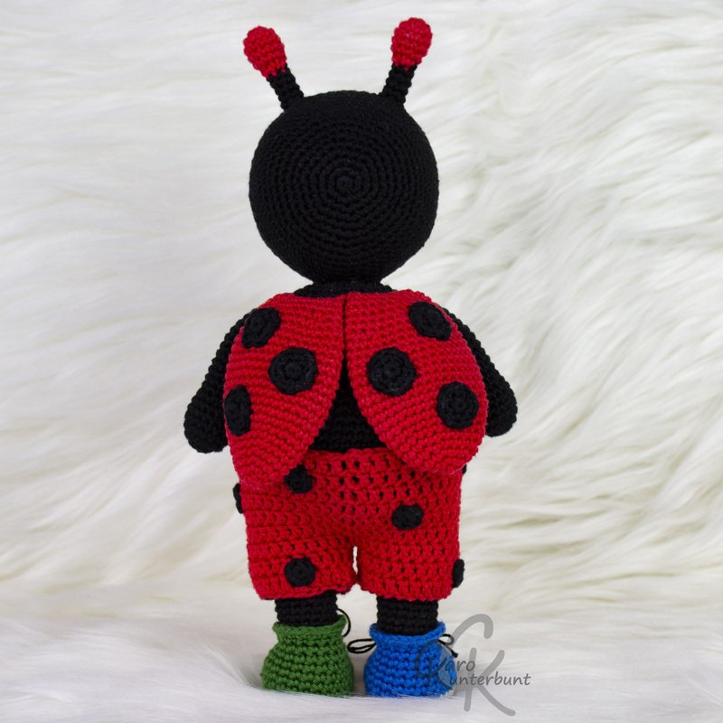 Rückansicht eines gehäkelten Marienkäfer-Amigurumi mit roten Flügeln und schwarzen Punkten