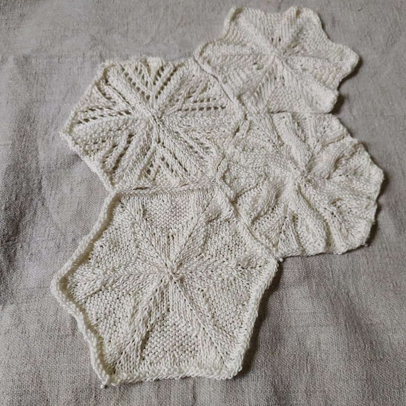 Gestrickte sechseckige Motive aus hellem Garn mit sternförmigem Muster auf Leinen