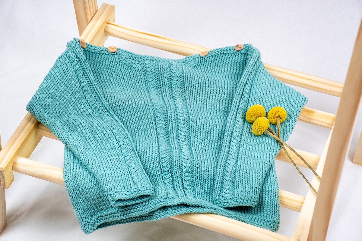Türkiser gestrickter Baby-Pullover mit Schulterknöpfen auf Holzgestell