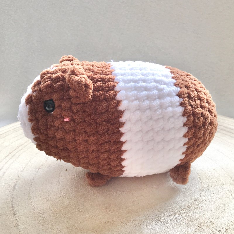 Gehäkeltes Meerschweinchen-Amigurumi in Braun und Weiß auf Holzuntergrund