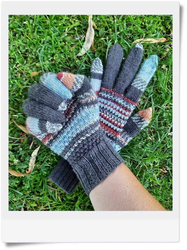 Gestrickte graue Damenhandschuhe mit mehrfarbigen Streifen auf Gras