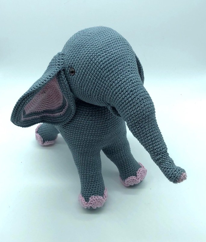 Gehäkelter grauer Amigurumi-Elefant mit rosa Innenohren und Zierkanten, stehende Ansicht