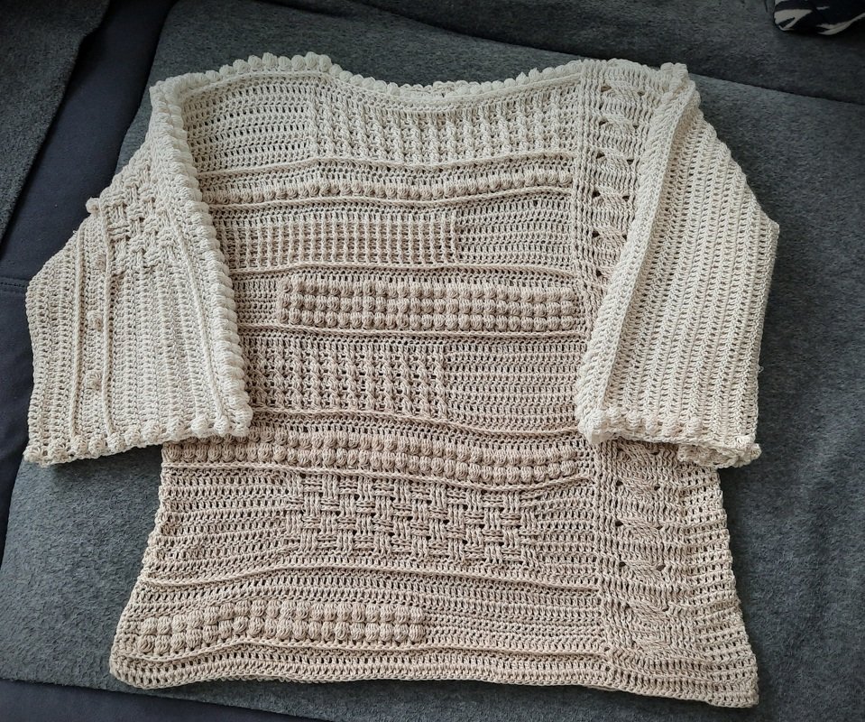 Beiger handgehäkelter Damenpullover mit Noppen-, Relief- und Zopfmustern und 3/4-Ärmeln, flach ausgelegt.