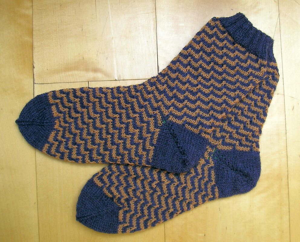Gestrickte Herrensocken in Blau und Braun mit Zickzackmuster auf Holzuntergrund
