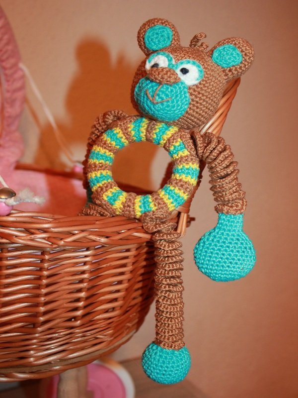 Gehäkelter braun-türkiser Affe mit gestreiftem Rasselring im Weidenkorb