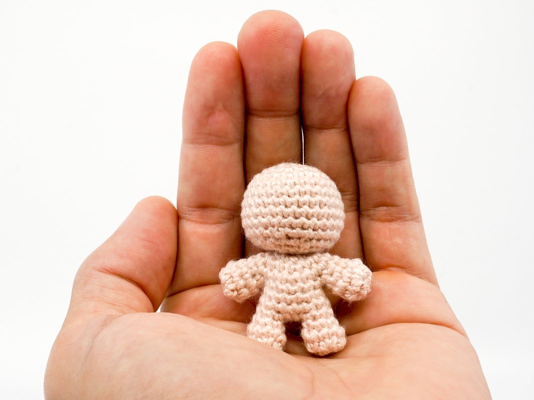 Kleiner beiger gehäkelter Amigurumi-Rohling in einer Hand
