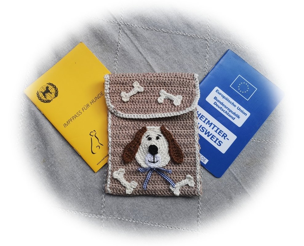 Beige gehäkelte Hülle mit Hundegesicht und Knochen-Applikationen, daneben Impfpass und Heimtierausweis