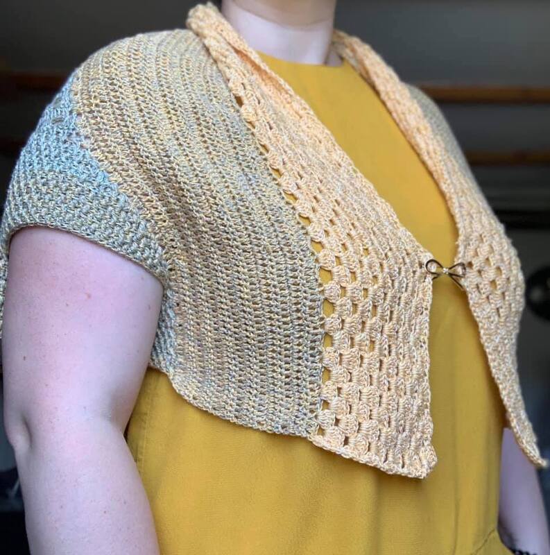 Gehäkelter Kurzbolero in Gelb‑Beige mit kurzer Ärmel und dekorativer Metallschließe über senffarbenem Top