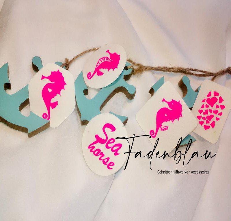 Hellblaue Ankeranhänger mit weißen Etiketten, darauf neonpinke Seepferdchen- und Herz-Silhouetten sowie ein 'Sea horse' Schriftzug, auf hellem Hintergrund
