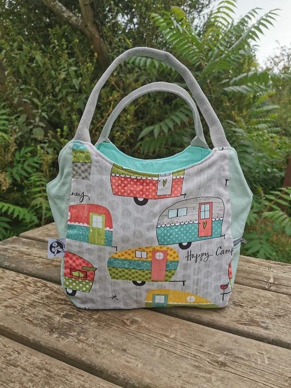 Bunte genähte Einkaufstasche aus Stoff mit Wohnwagen-Print, grauen Henkeln und türkisfarbenem Einsatz auf einer Holzbank