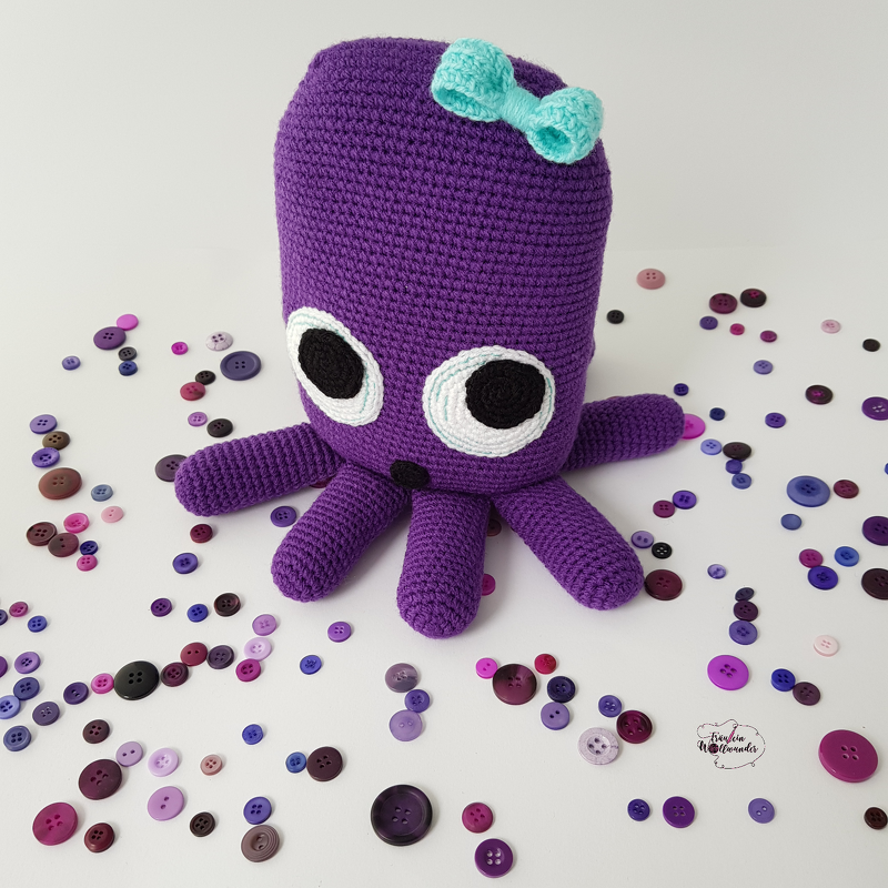 Lila gehäkelter Amigurumi-Oktopus mit hellblauer Schleife und bunten Knöpfen