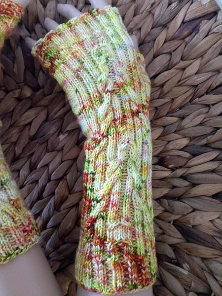Fingerlose, gestrickte Armstulpen in Herbstfarben mit Zopfmuster auf geflochtenem Untergrund.