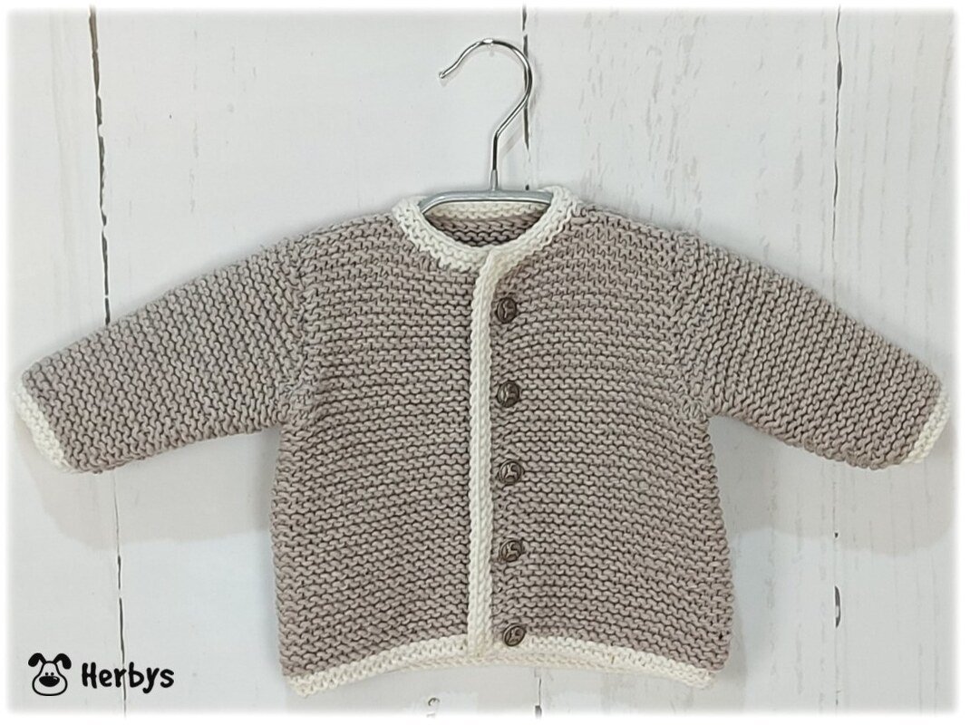 Handgestrickte Babyjacke in Beige mit cremeweißer Einfassung auf Kleiderbügel