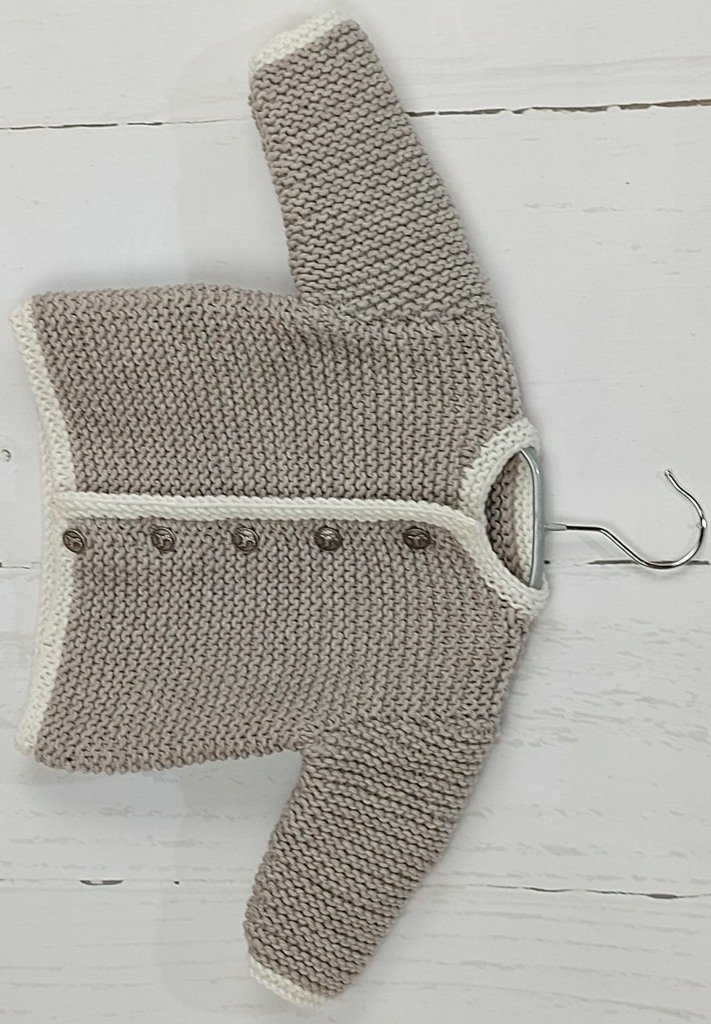 Gestrickte beige Babyjacke mit weißer Einfassung und fünf Knöpfen auf einem Bügel