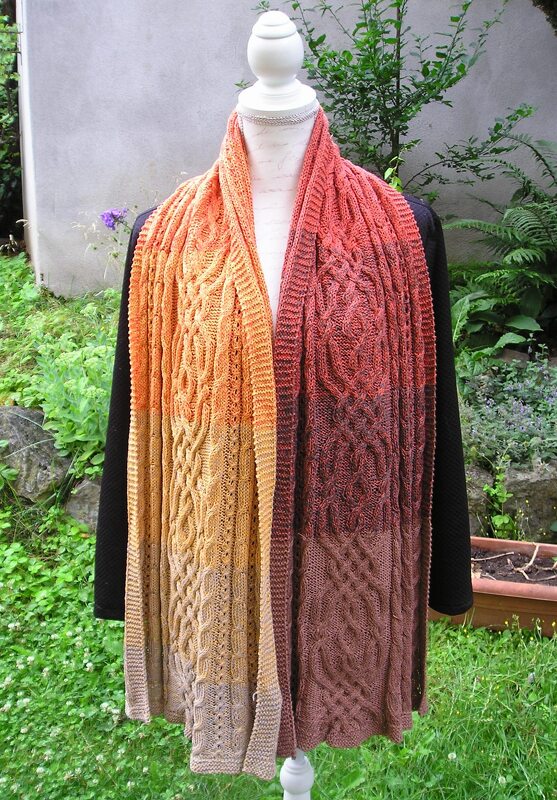 Mannequin trägt langen gestrickten Schal mit Zopfmuster und gelb-orangem bis braunem Farbverlauf