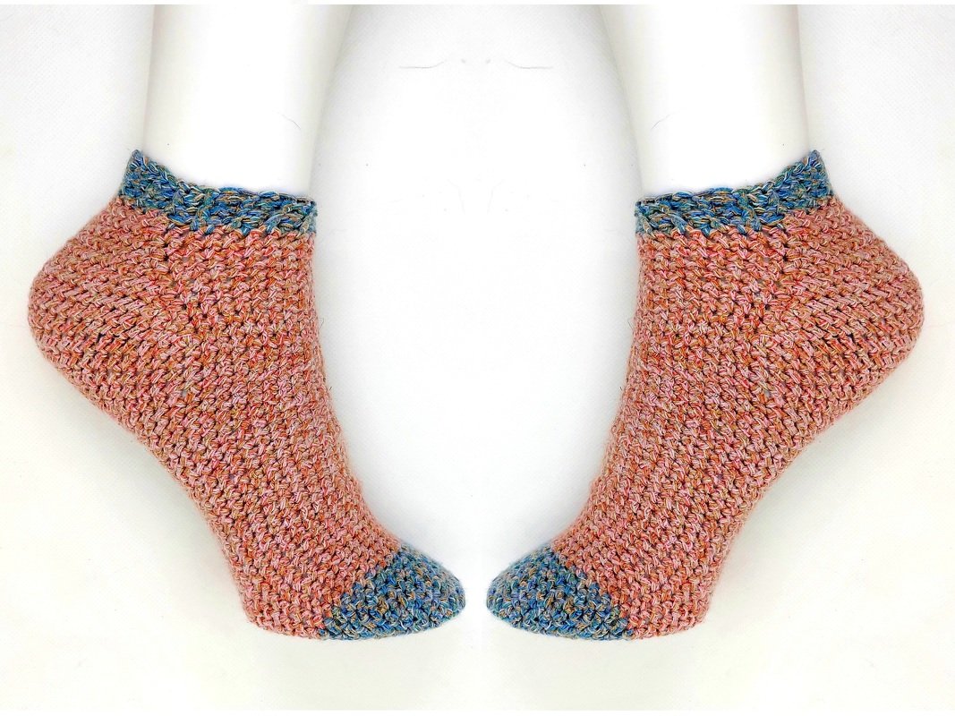 Nahaufnahme zweier kurzer gehäkelter Socken in Rosé mit blauem Bündchen und blauer Spitze