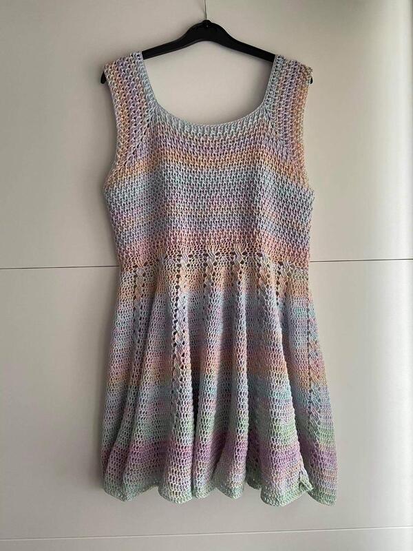 Ärmelloses gehäkeltes Damenkleid in zartem Pastellverlauf mit eckigem Ausschnitt und ausgestelltem Rock an einem Bügel.