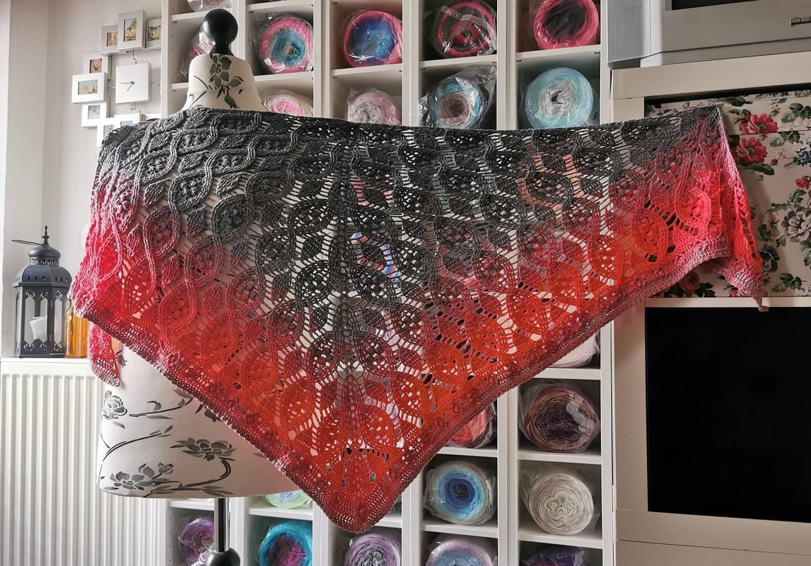 Crocheted triangle shawl with a dark-grey to red-orange gradient and openwork lace motif draped on a mannequin.