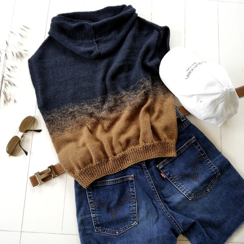 Flat lay of a knitted sleeveless cowl neck top in a blue-to-brown gradient with denim shorts, belt, and sunglasses.