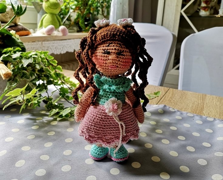 Gehäkelte Amigurumi-Puppe mit braunen Locken, mintgrünem Kragen und rosa Häkelrock mit Blüte