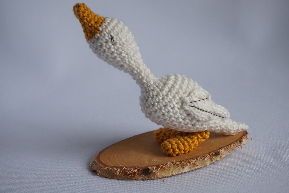 Gehäkelte weiße Gans mit orangefarbenem Schnabel und Füßen auf einer runden Holzscheibe