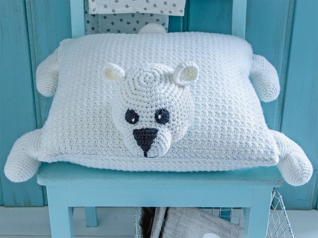 Weißes, gehäkeltes Eisbär-Kissen mit dunklen Augen und Nase auf hellem, blauem Stuhl