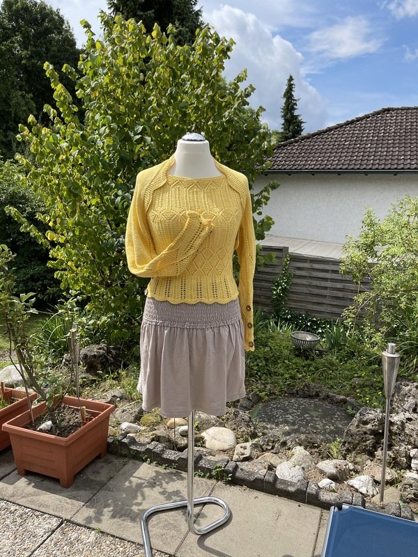 Mannequin mit gelbem Strickoberteil mit Lochmuster und hellem Rock im Garten