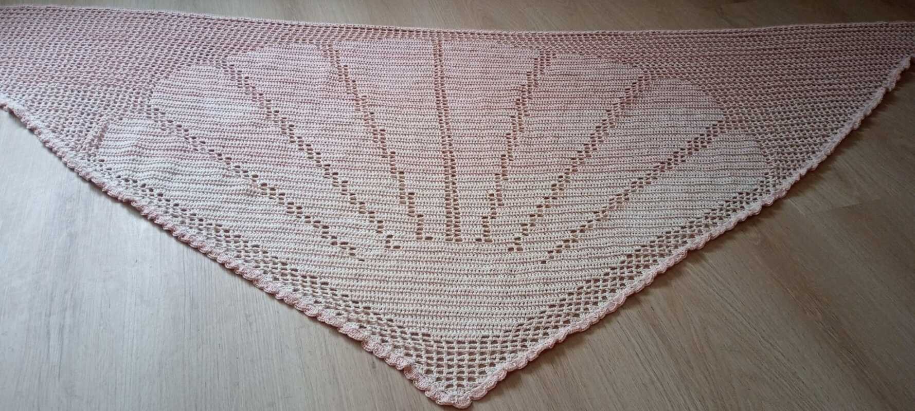 Zartrosa gehäkeltes Dreieckstuch mit Fächermuster, liegend auf Holz