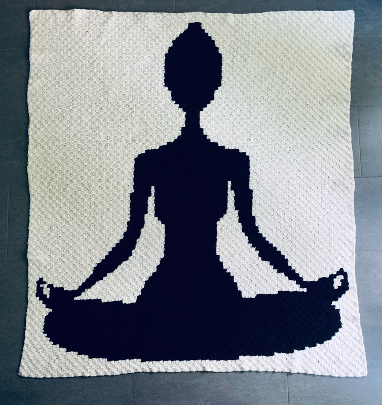 Gehäkelte weiße Decke mit schwarzer Silhouette einer meditierenden Person im Lotussitz.