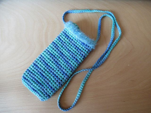 Gehäkelte gestreifte Tasche in Blau und Türkis mit flauschigem Rand und langem Riemen auf Holztisch.