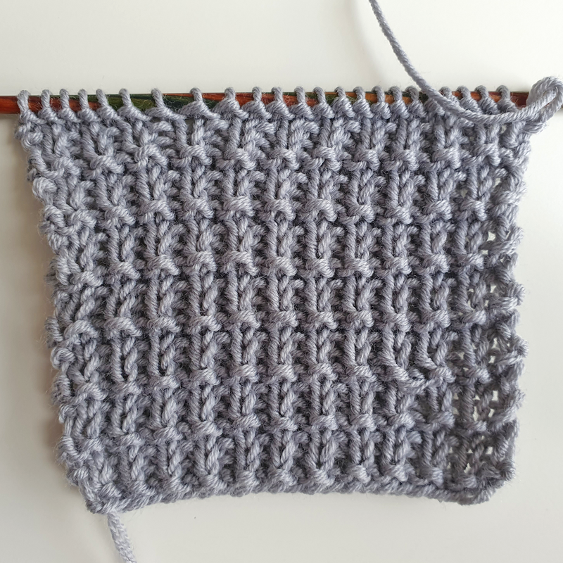 Grau texturiertes Strickmuster als Inspirationsprobe, teilweise auf Stricknadeln
