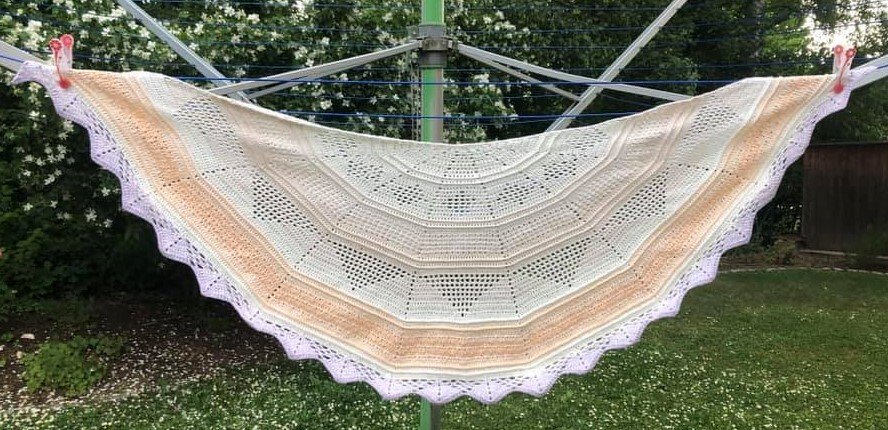 Gehäkeltes Halbrundtuch in Creme, Pfirsich und Flieder mit gezacktem Spitzenrand an einer Wäschespinne
