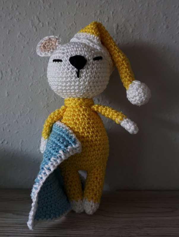 Crocheted yellow amigurumi bear wearing nightcap and holding a blue blanket