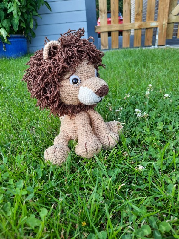 Gehäkelter Amigurumi-Löwe mit brauner Mähne sitzt im grünen Gras