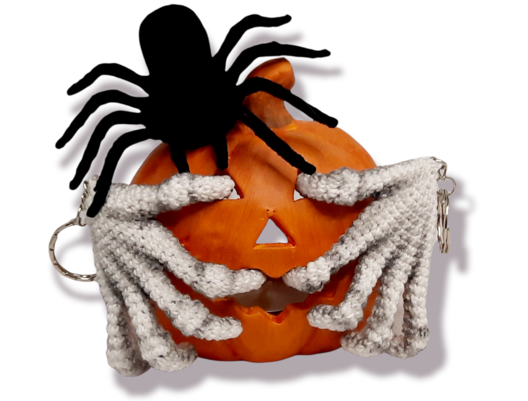 White crocheted skeleton hand keychains with metal rings beside a carved pumpkin and a black spider