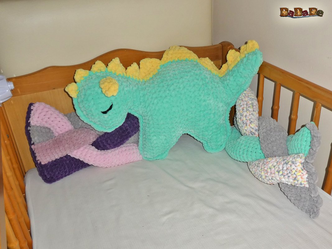 Gehäkeltes mintgrünes Dino-Kissen mit gelben Stacheln im Holz-Kinderbett