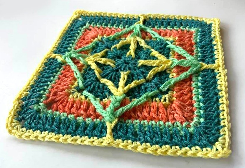 Gehäkeltes Quadrat mit reliefartigem Stern‑Kreuz‑Muster in Türkis, Koralle, Hellgrün und Gelb.