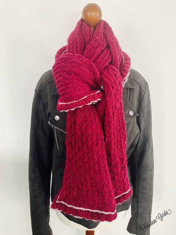 Bordeauxroter Strickschal mit strukturiertem Muster und hellem Rand, um eine Schaufensterpuppe gelegt.