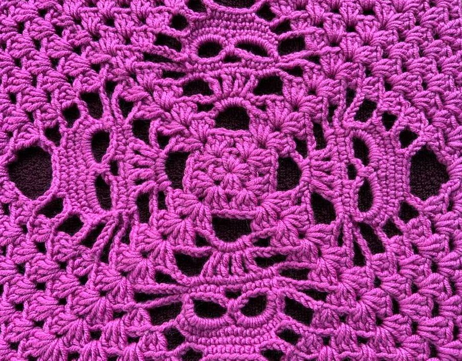 Gehäkeltes Muster in Fuchsia mit offenen Maschen und stern- sowie ovalen Aussparungen.