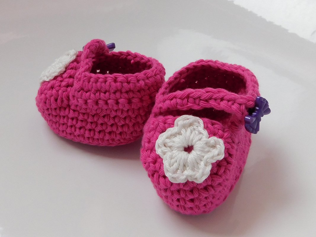 Fuchsiafarbene gehäkelte Baby-Ballerinas mit weißer Häkelblüte und lila Knopf