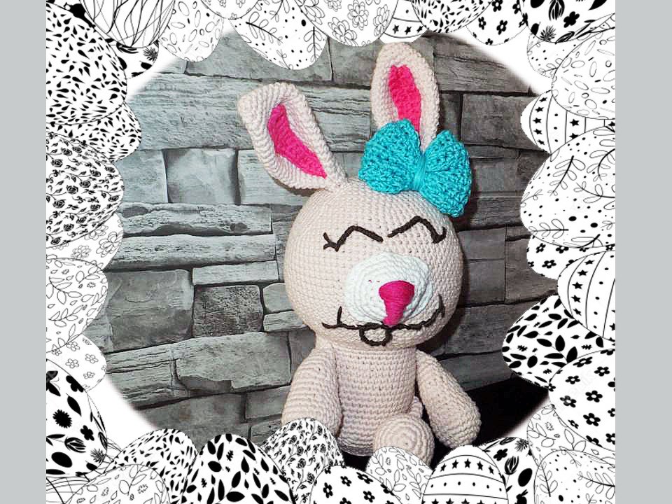 Gehäkelter beiger Amigurumi-Hase mit pinken Ohren und türkisfarbener Schleife, umrahmt von schwarz-weißen Ostereiern