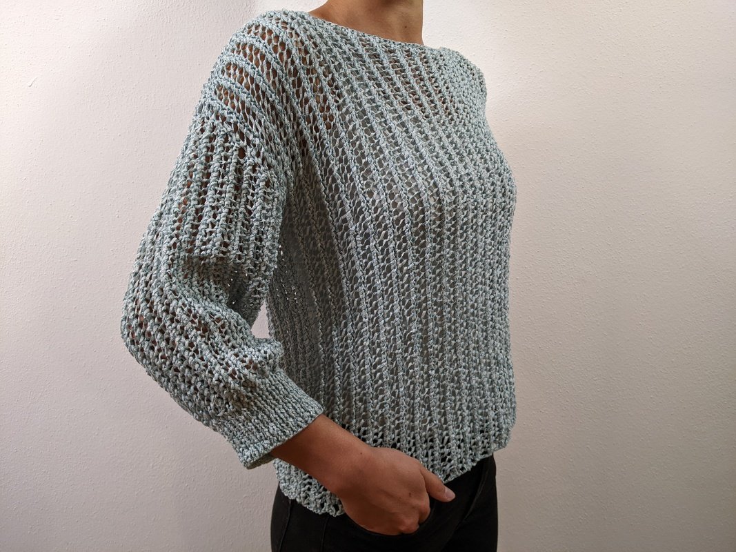 Seitliche Ansicht eines salbeigrünen Damenpullovers mit lockerem Ajour‑Lochmuster und schmalen Bündchen