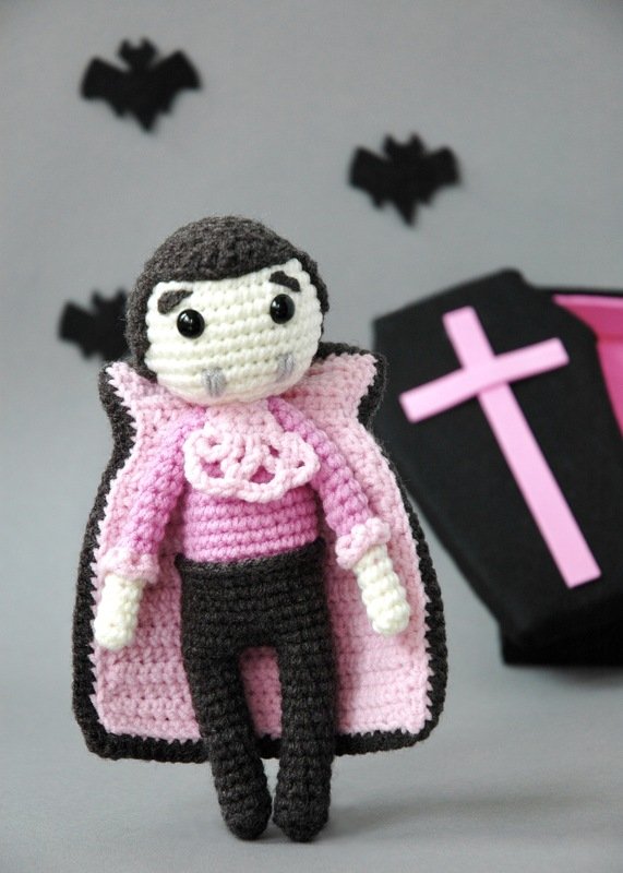 Crocheted vampire amigurumi in black and pink with ruffled collar and pink-lined cape