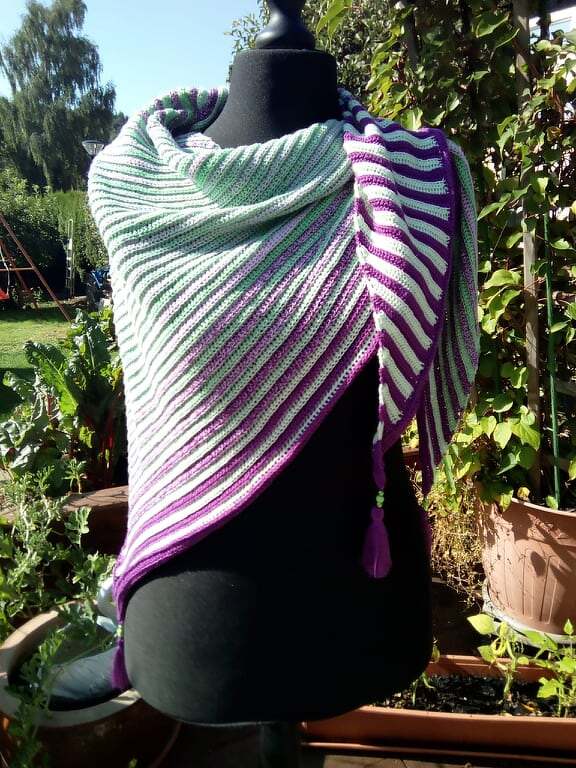 Gehäkeltes Dreieckstuch in Mint, Weiß und Lila mit diagonalem Streifenmuster und Quaste auf schwarzer Schneiderpuppe im Garten